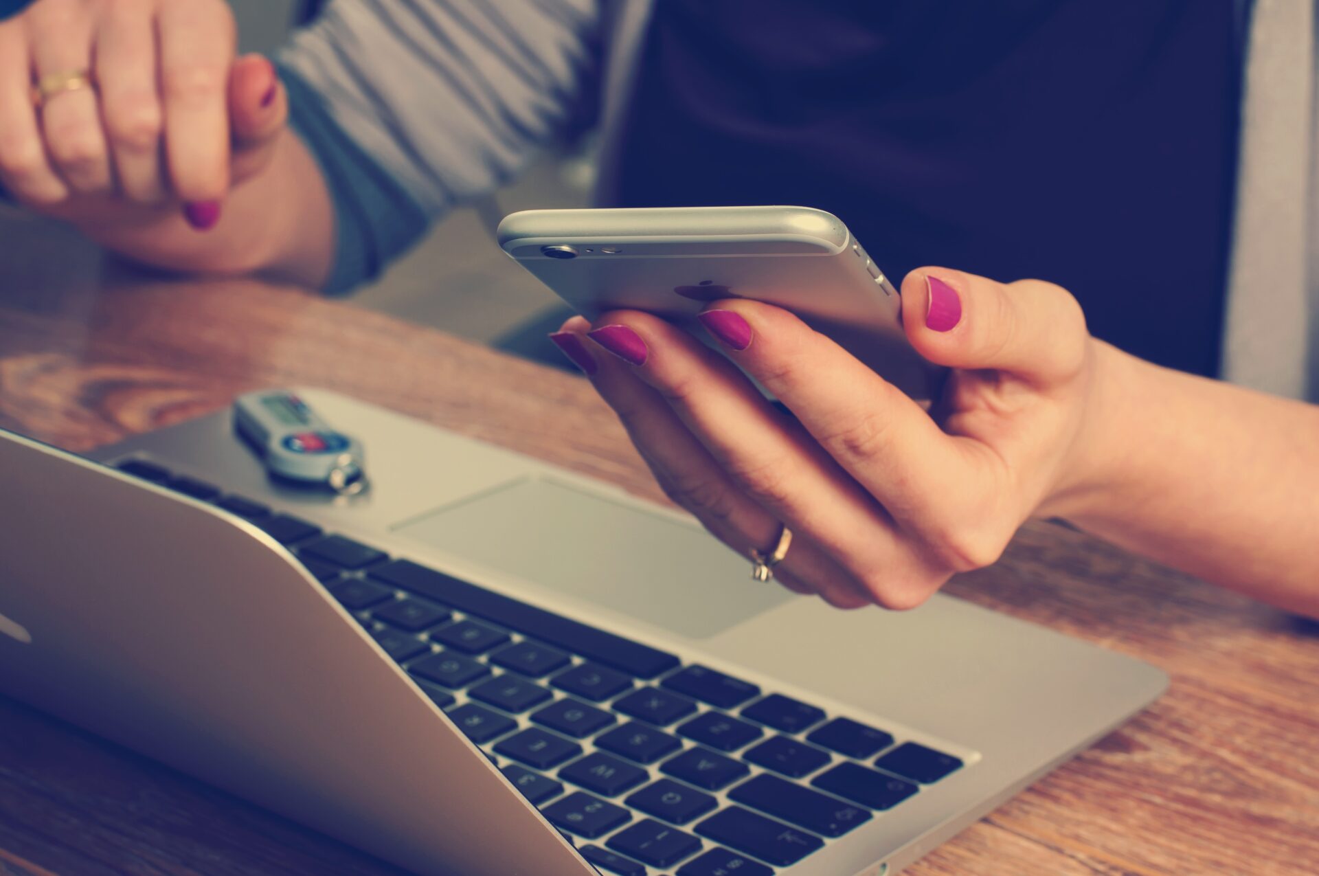 A woman holding a cell phone next to a laptop.