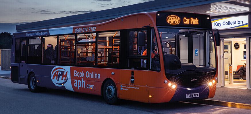 An orange and white bus is parked outside a store.
