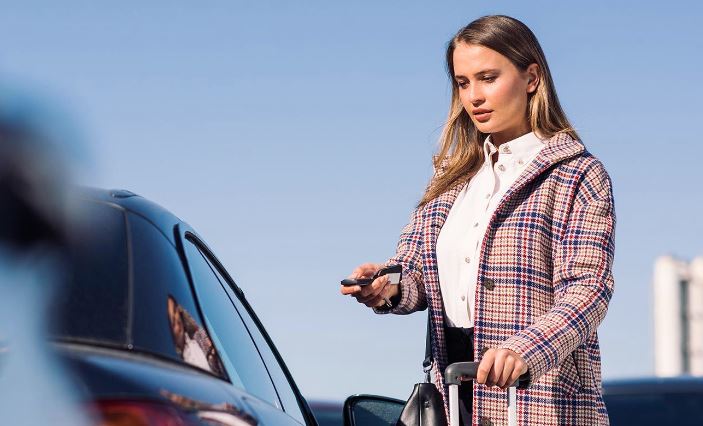 A woman is standing next to her car and holding her phone.