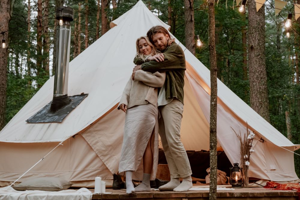 Couple embracing in front of a tent in the woods.