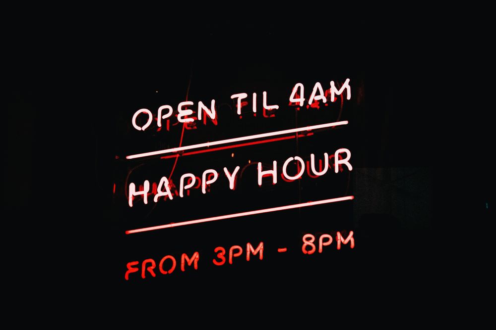 A neon sign that reads open til am happy hour.