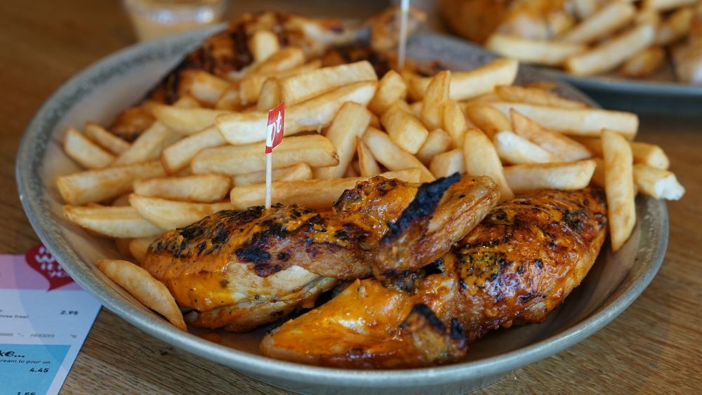 A bowl of grilled chicken and french fries on a table.