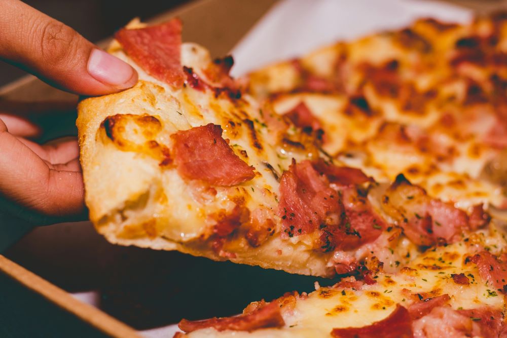 A person taking a slice of pizza out of a box.