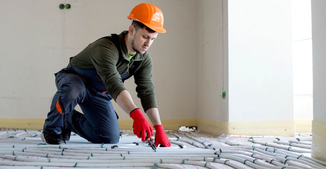 A man in a hard hat working on pipes for underfloor heating