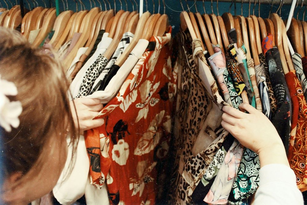 A woman is choosing clothes from a rack of clothes.
