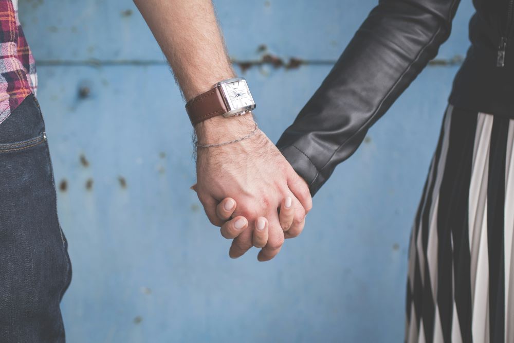 A man and woman holding hands in front of a blue wall.