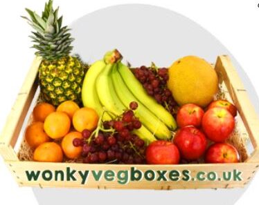 fruit box A wooden crate filled with various fruits including a pineapple, bananas, apples, grapes, oranges, and a melon. The crate has the text "wonkyvegboxes.co.uk" on the front.