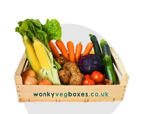 veggie box A wooden crate labeled "wonkyvegboxes.co.uk" contains various vegetables including lettuce, corn, carrots, zucchini, potatoes, onions, tomatoes, and a purple cabbage.