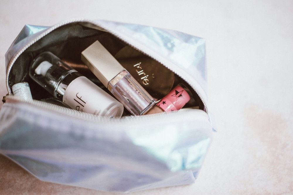 Apps that pay you to help the planet A metallic makeup bag partially unzipped, containing various makeup products such as foundation, concealer, and lip gloss.