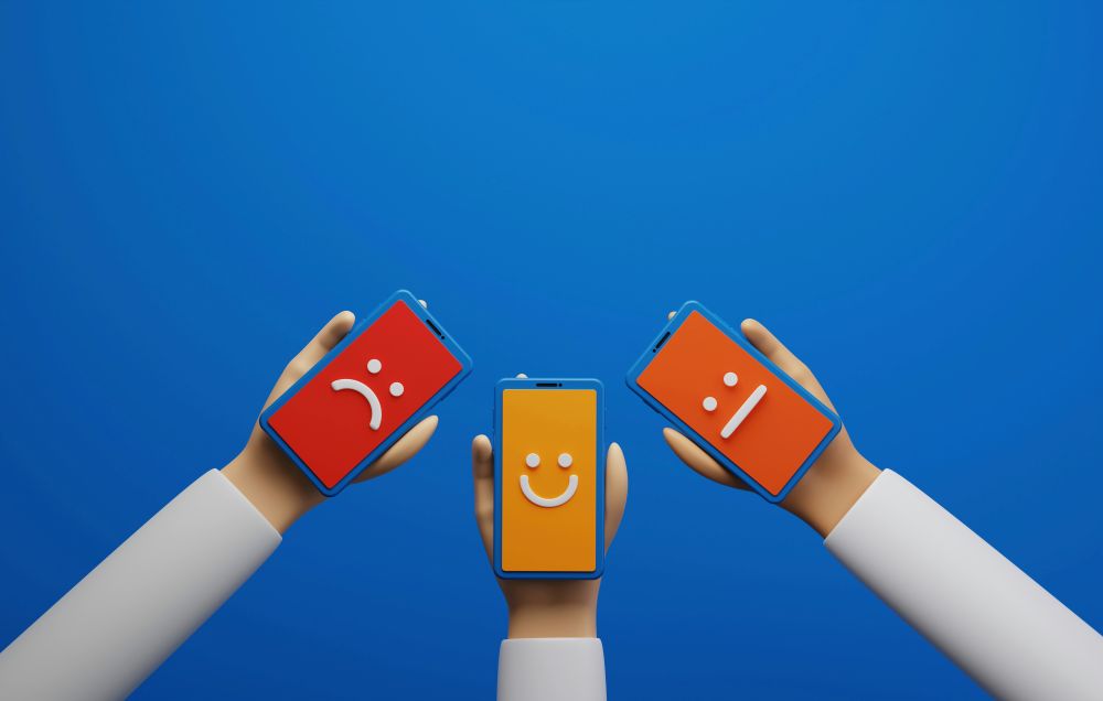 Money making apps Three cartoon hands holding smartphones display different face emojis: sad (left), happy (center), and neutral (right), against a plain blue background.