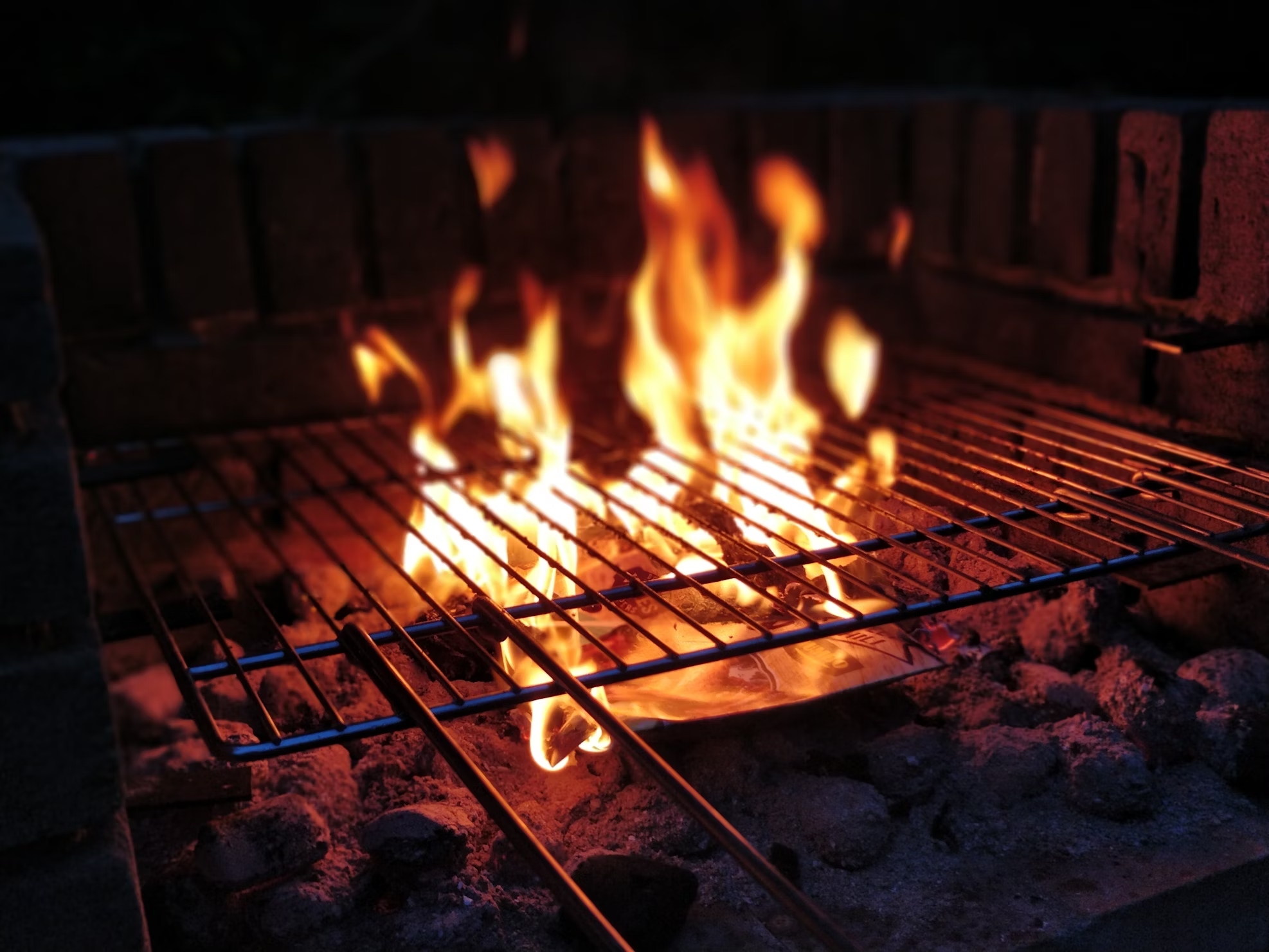 Charcoal barbecue Flames rise from a charcoal BBQ grill with an empty cooking grate, surrounded by brick sides, ready for food to be cooked.