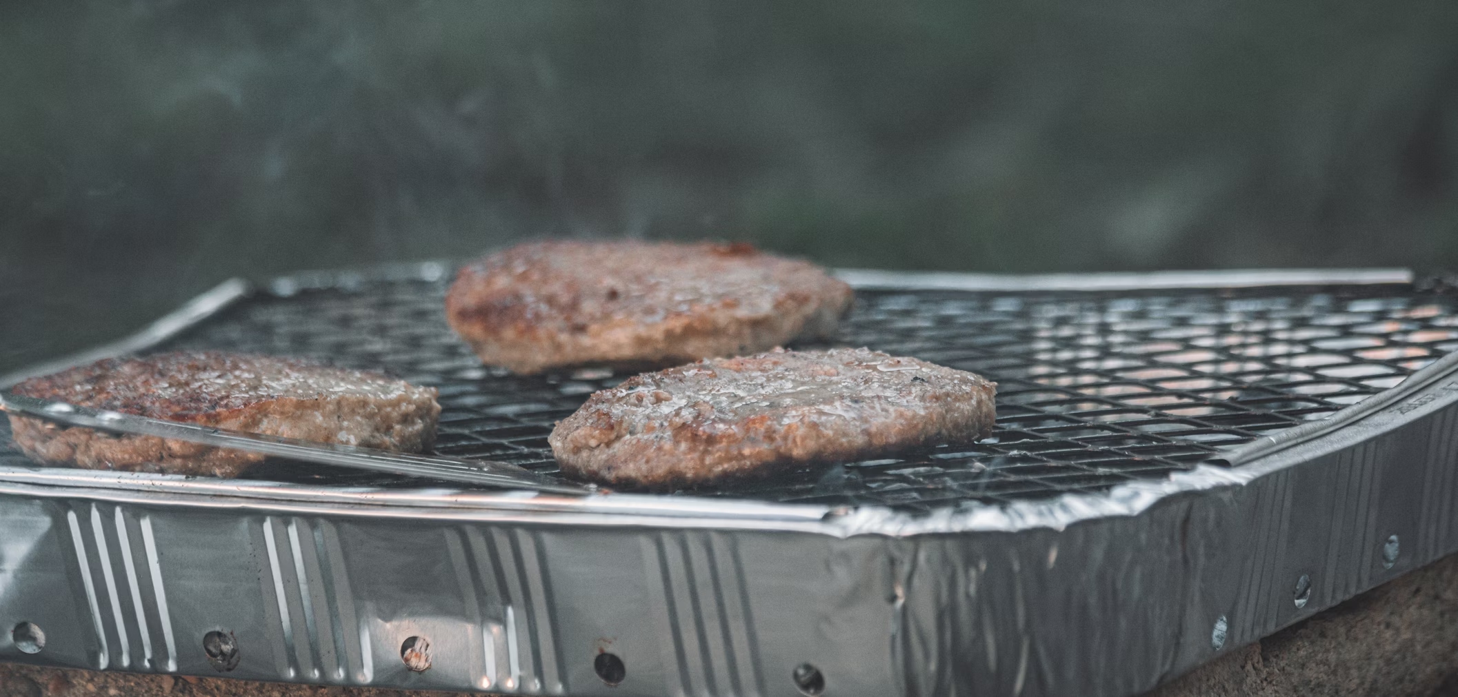 Disposable BBQ Three beef burgers cooking on a disposable BBQ grill