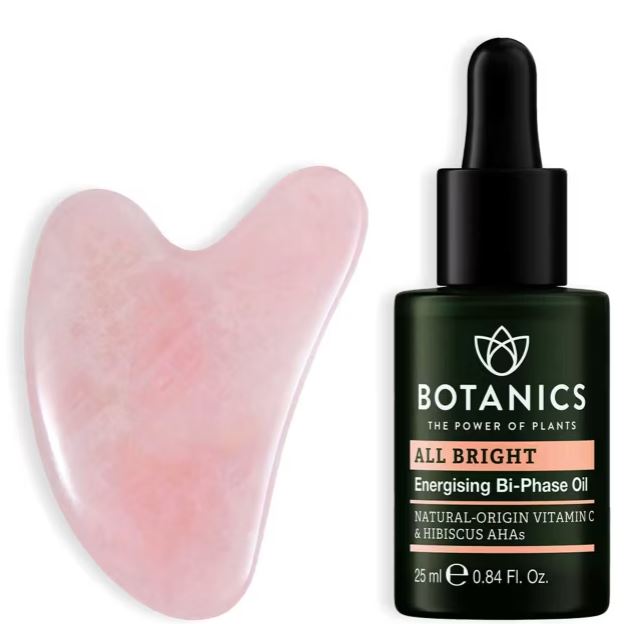 A pink gua sha stone is next to a 25ml bottle of Botanics All Bright Energising Bi-Phase Oil with a dropper lid.
