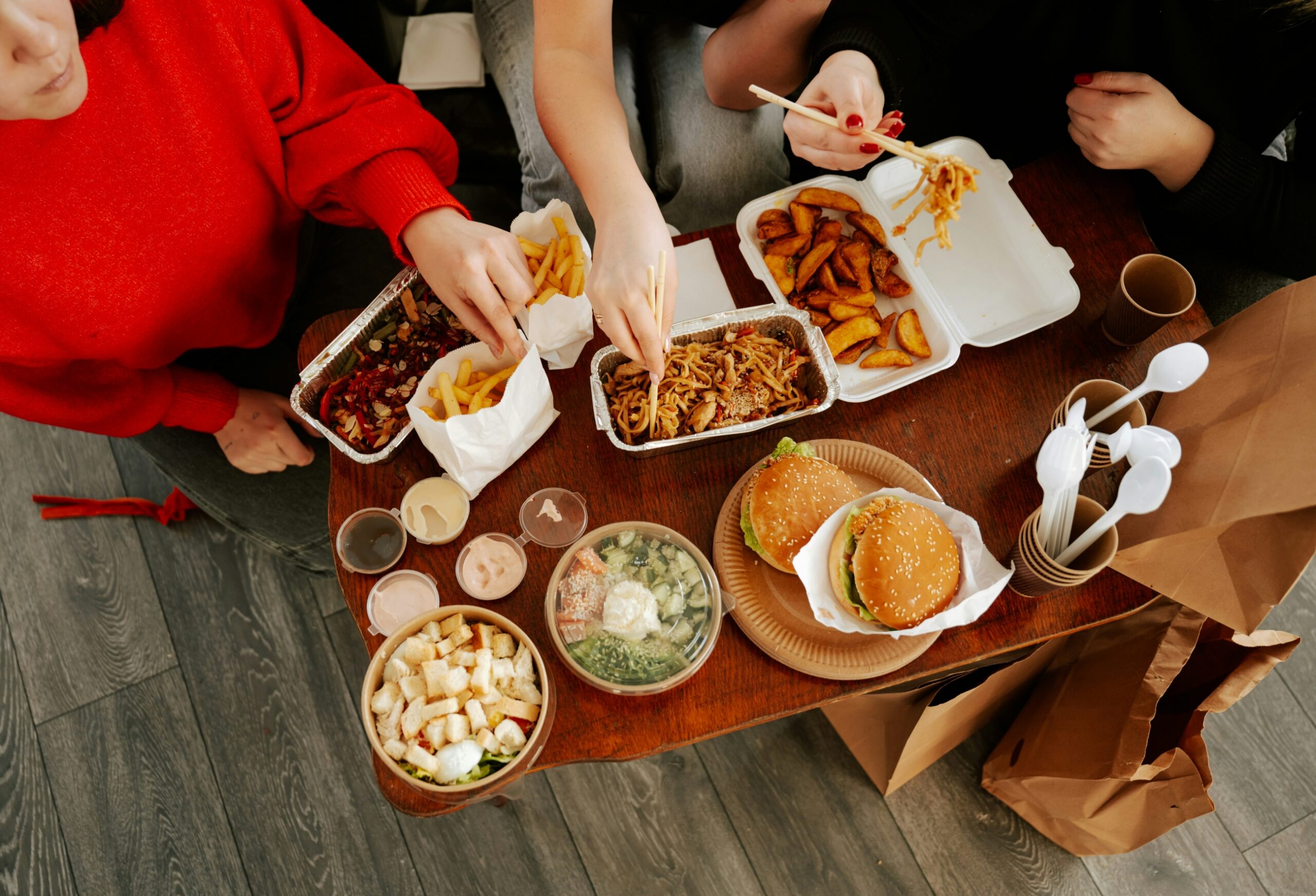 takeaway burgers Three people eating takeaway food including fries, burgers, and pasta