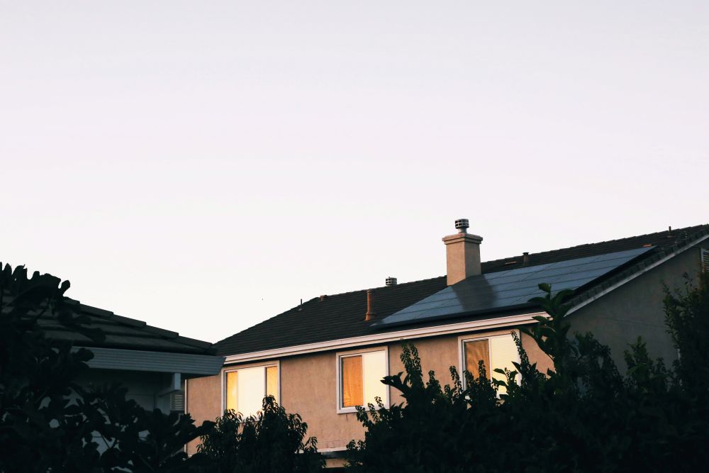 House with solar panels installed House with solar panels on the roof, partially obscured by trees, photographed at sunset with a clear sky in the background.