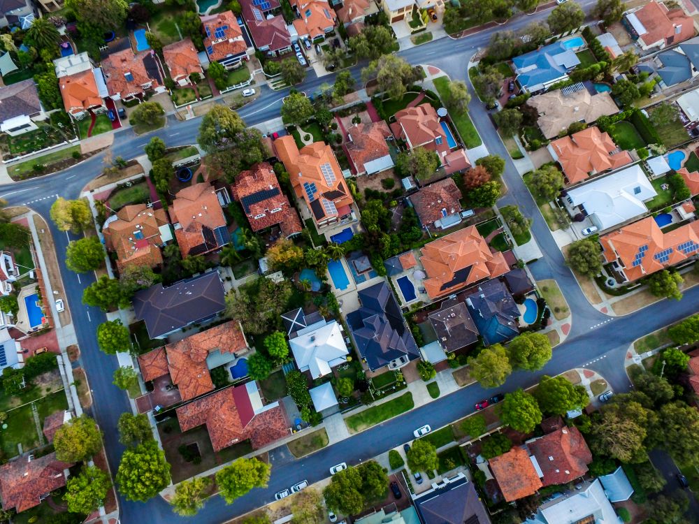 Houses from above Aerial view of a suburban neighborhood showing houses with red and gray roofs, tree-lined streets, and several visible swimming pools.