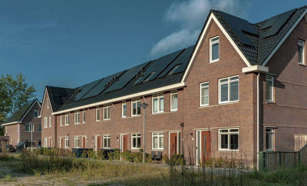 Houses with solar panels Row of modern brick townhouses with large windows and dark roofs under a clear sky, with some grass and shrubs in the foreground.