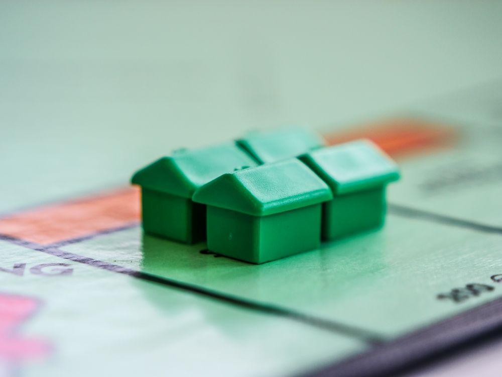 Four green plastic houses are placed on a Monopoly board near the edge of a property space, ready to unlock McDonald's rewards just like collecting those free McDonald's tokens in the game.