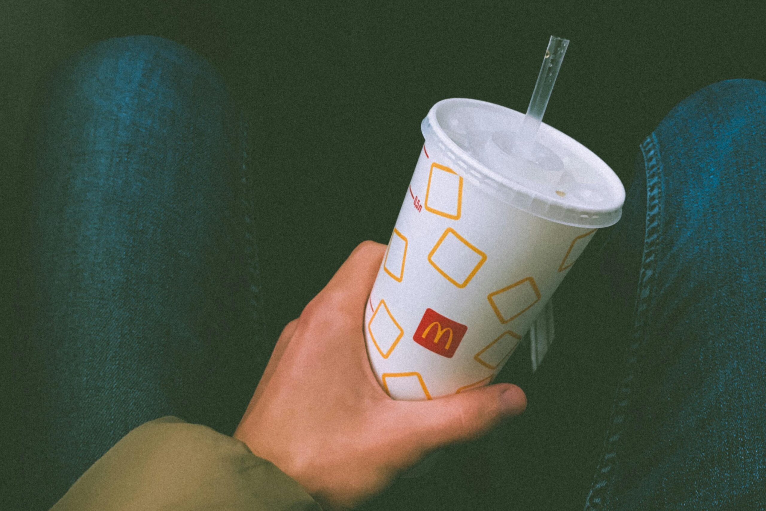 A hand holding a paper cup with a straw, ready to enjoy refreshing sips—perfect for redeeming McDonald's rewards on your next visit.