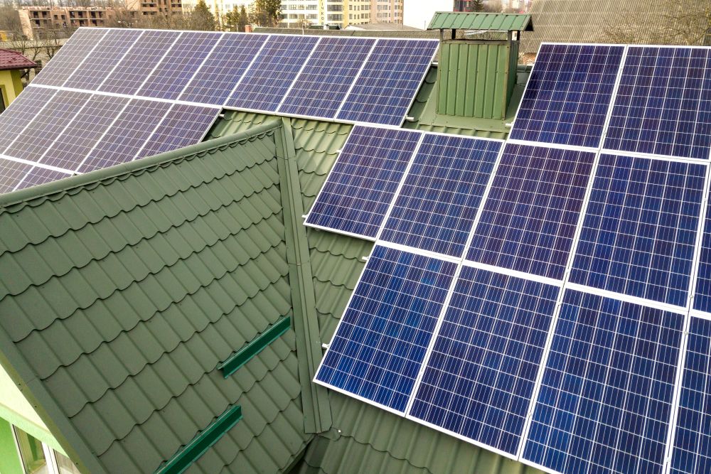 Polycrystalline panels Solar panels are installed on the green metal roof of a building, arranged in several rows to capture sunlight for energy generation.