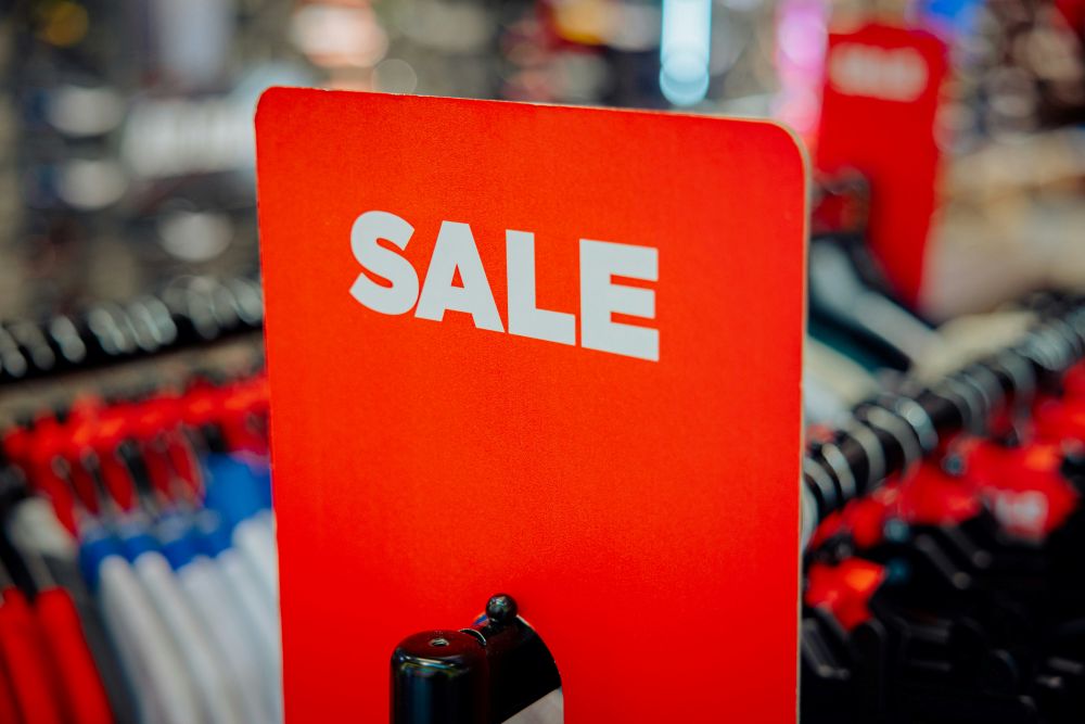 A red sign with the word "SALE" in white letters is displayed in front of clothing racks, inviting Brits to discover a great bargain promotion in the store.