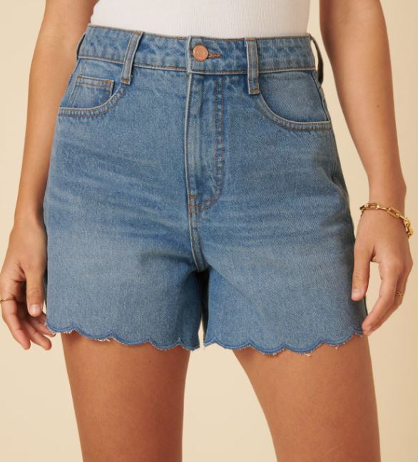 Person wearing high-waisted blue denim shorts with scalloped hems, a white top, and a gold bracelet.