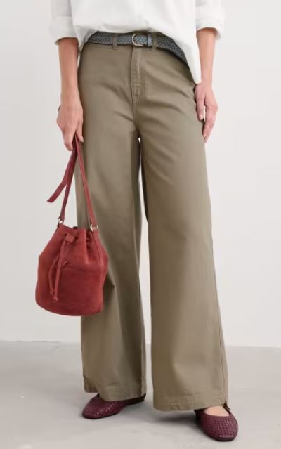 Person wearing wide-leg khaki pants, a white shirt, braided belt, holding a red suede bucket bag, and wearing maroon flats.