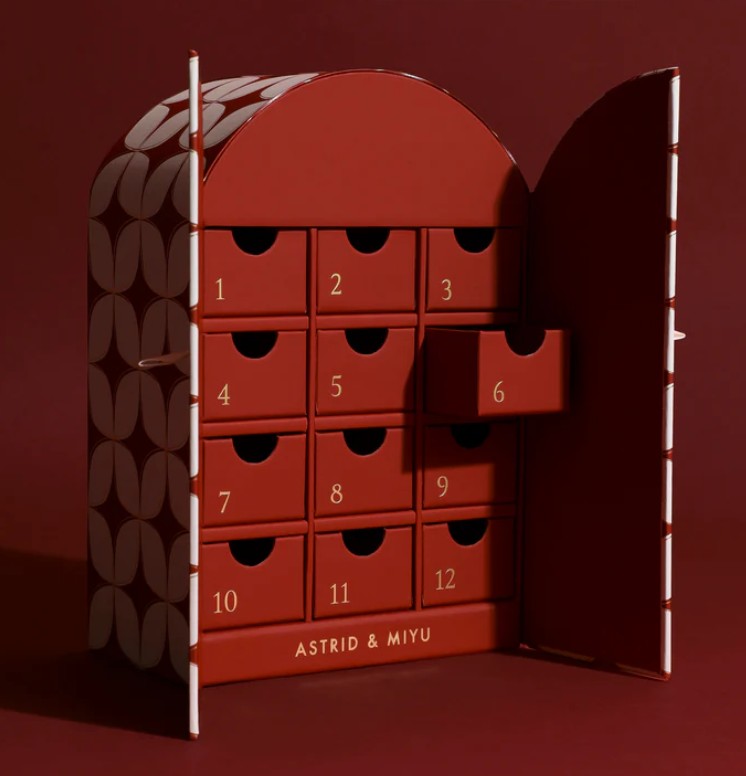 Astrid & Miyu 12-Day Advent Calendar 2025 A red box with numbered drawers from 1 to 12, one drawer partially open, labeled “ASTRID & MIYU” on the front, against a dark red background.