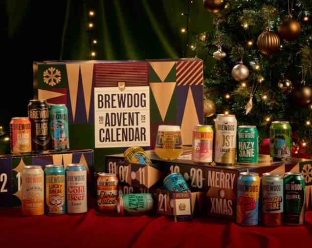A BrewDog Advent Calendar box is displayed with various BrewDog beer cans in front, next to a decorated Christmas tree on a red cloth background.