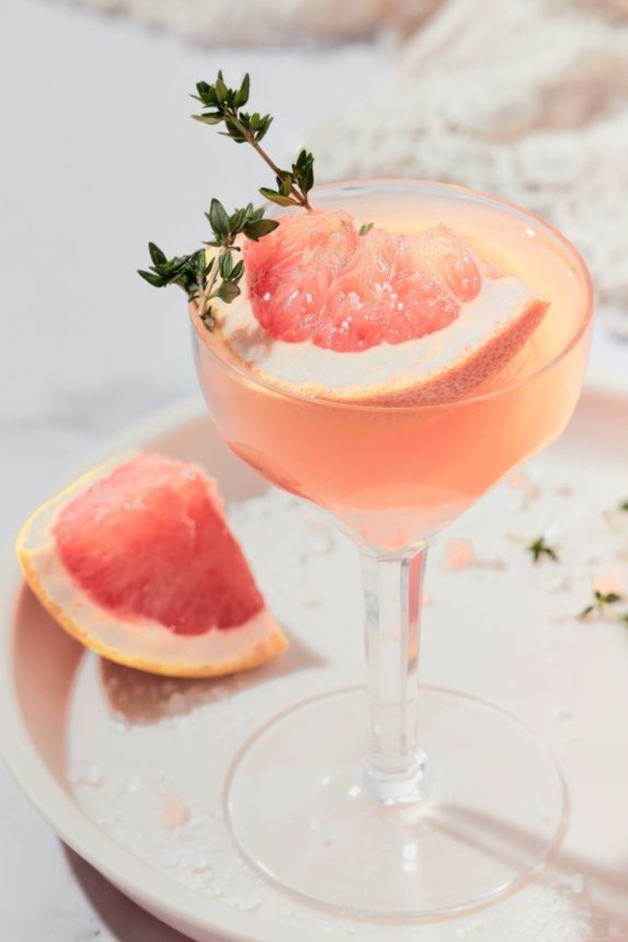 A glass with a drink and a slice of grapefruit on it.