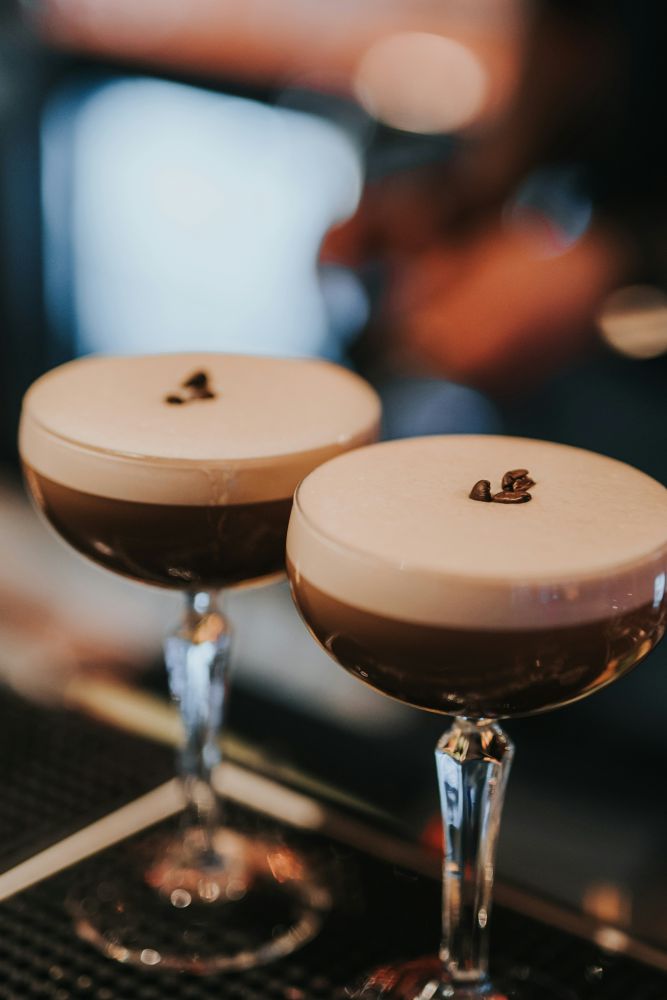 Two espresso martinis in coupe glasses, topped with a layer of foam and garnished with three coffee beans each.