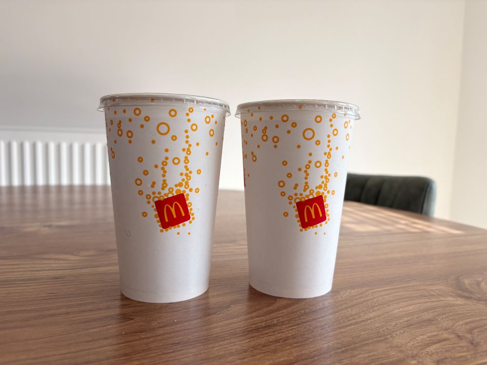 Two McDonald's paper cups with lids are placed side by side on a wooden table.