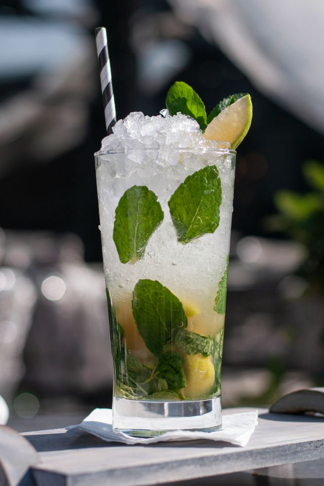 A tall glass filled with ice, lime wedges, fresh mint leaves, and a striped straw, placed on a napkin.