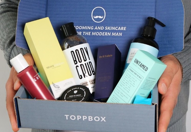 A person holds an open blue Toppbox containing assorted men's grooming and skincare products in various bottles and boxes.