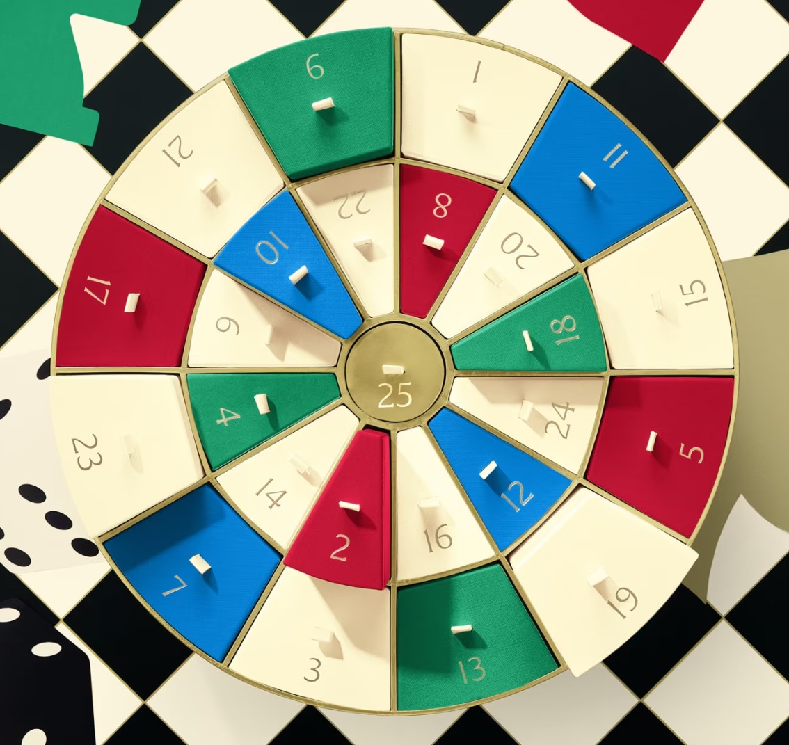 The Jo Malone London Advent Calendar 2025 A round advent calendar with numbered compartments in red, green, cream, and blue, arranged in concentric circles, displayed on a checkered background.