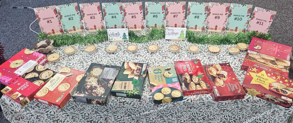 A table displays multiple boxes of mince pies, individual mince pies, green grass-like decorations, and winner signs labeled "Mince Pie #1" to "Mince Pie #11.