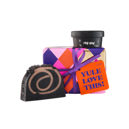 A small gift box with a purple ribbon, a dark swirl soap, and a black container labeled "Yog Nog." An orange tag on the box reads, "YULE LOVE THIS!.