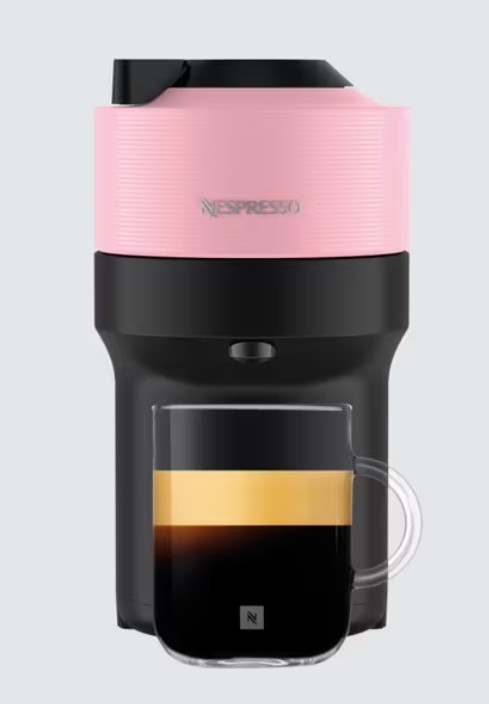 A pink and black Nespresso coffee machine with a clear glass cup filled with coffee placed underneath the dispenser.