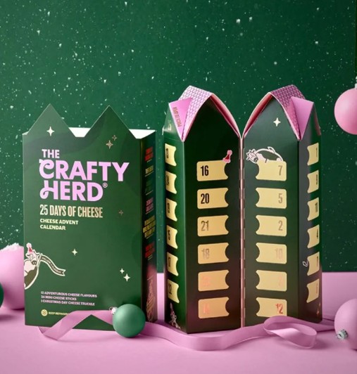 A green "Crafty Herd" cheese advent calendar is open, revealing numbered compartments for each day, against a festive background with ornaments.