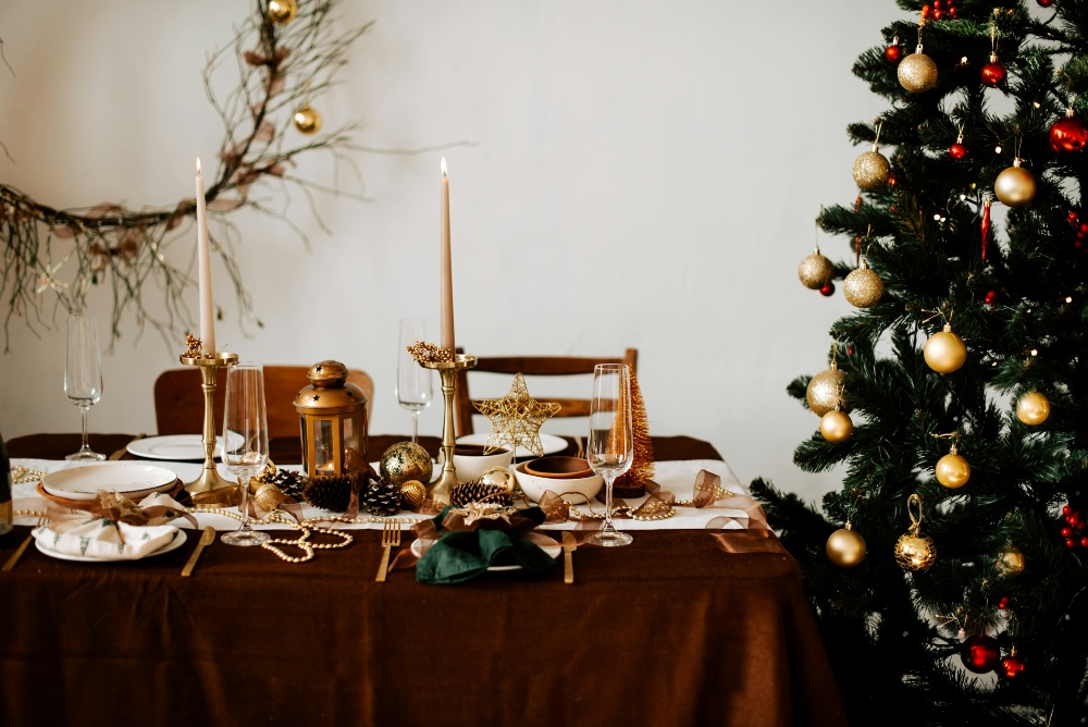Christmas table A festive dining table set with gold decorations and candles sits next to a decorated Christmas tree and a wall wreath with gold ornaments.