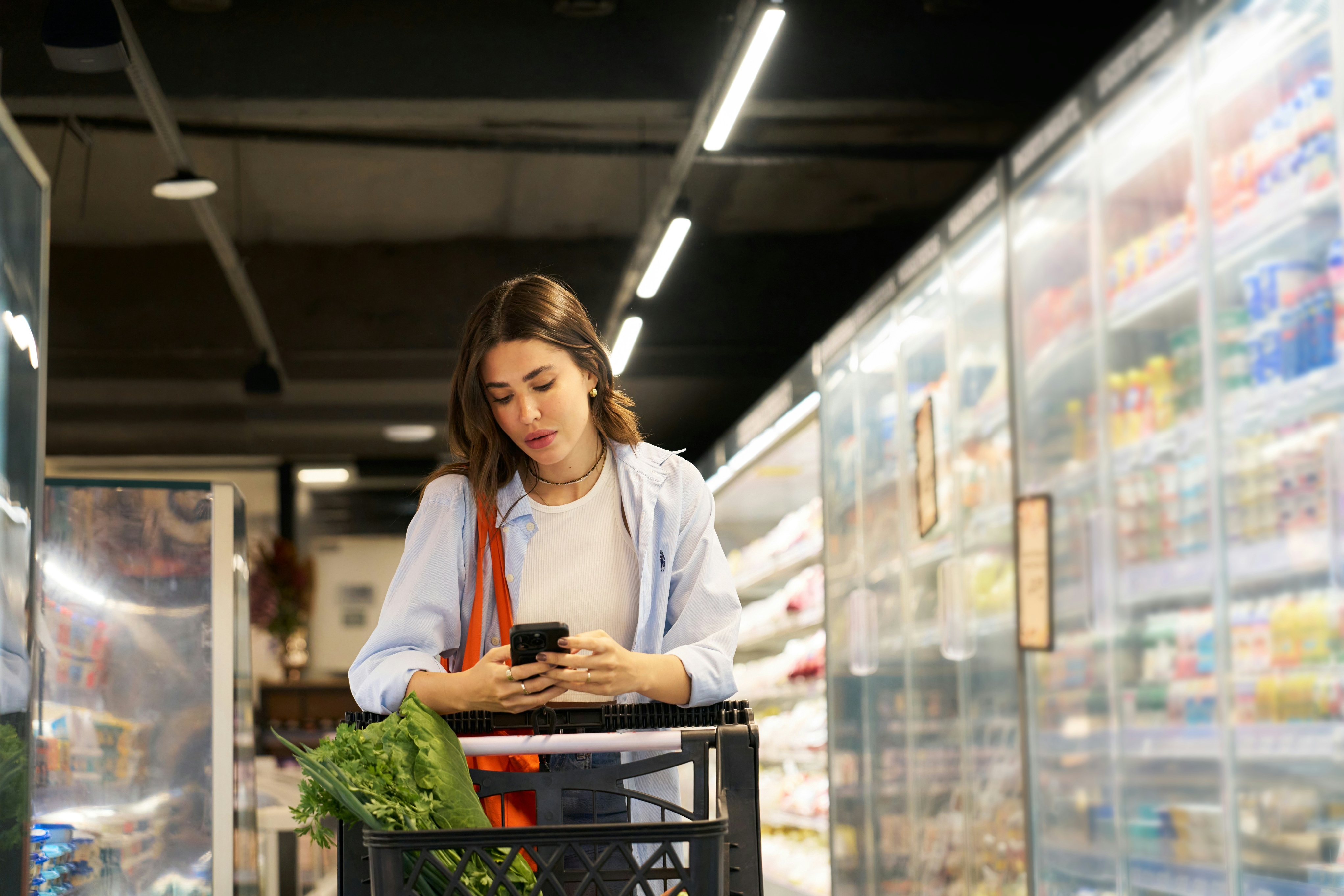 A woman standing by her shopping cart, reading her shopping list for supermarket dine-in deals