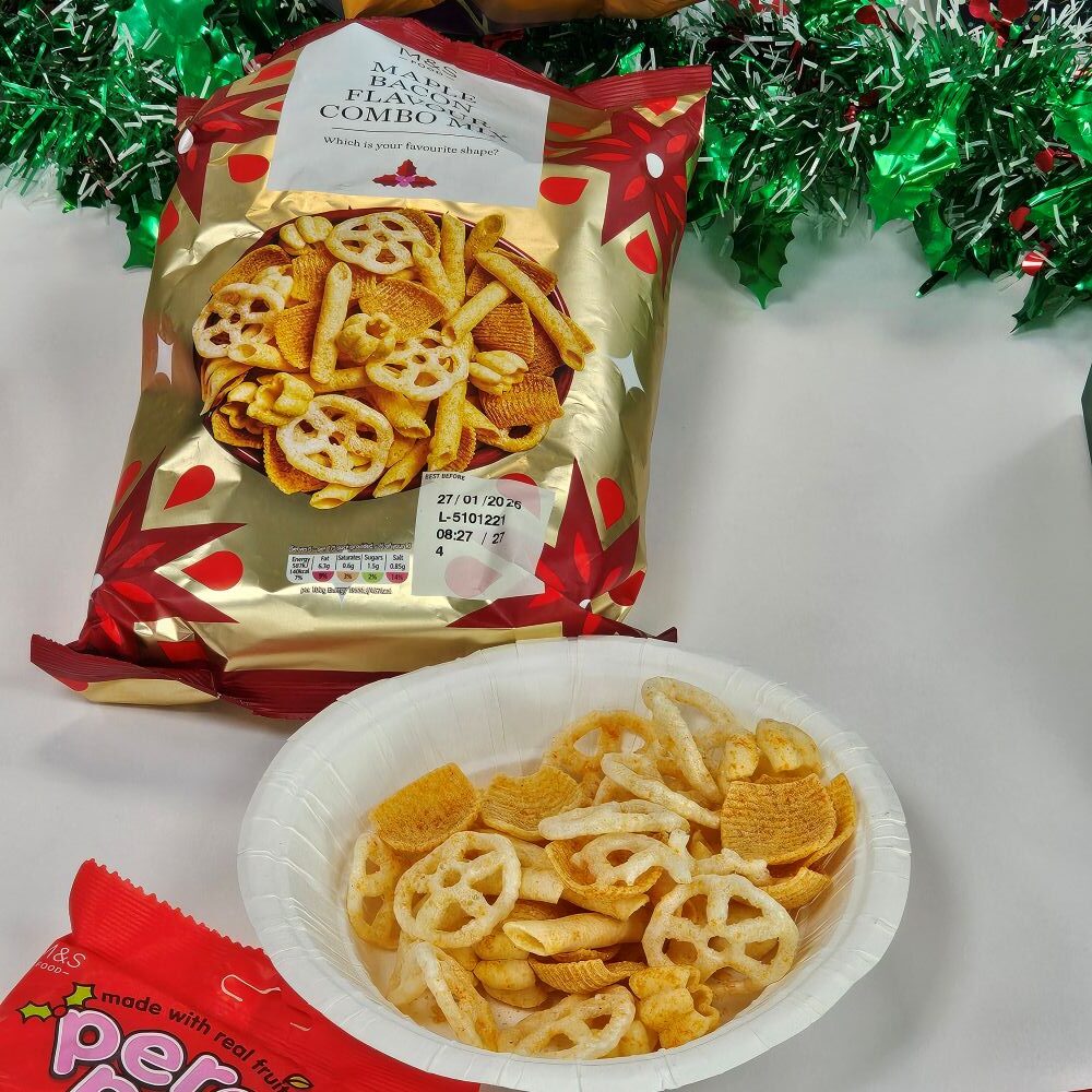 tcb marks and spencer maple bacon flavour combo mix A bowl of mixed vegetable snacks next to an open festive snack bag, with green and red tinsel decorations in the background.