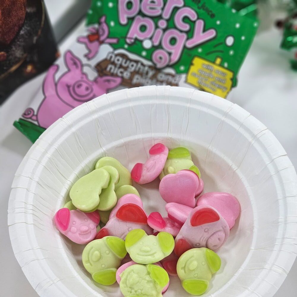 tcb marks and spencer percy pig naughty and nice piglets A paper bowl with pink and green pig-shaped gummy candies, with a bag labeled "Percy Pig" in the background.