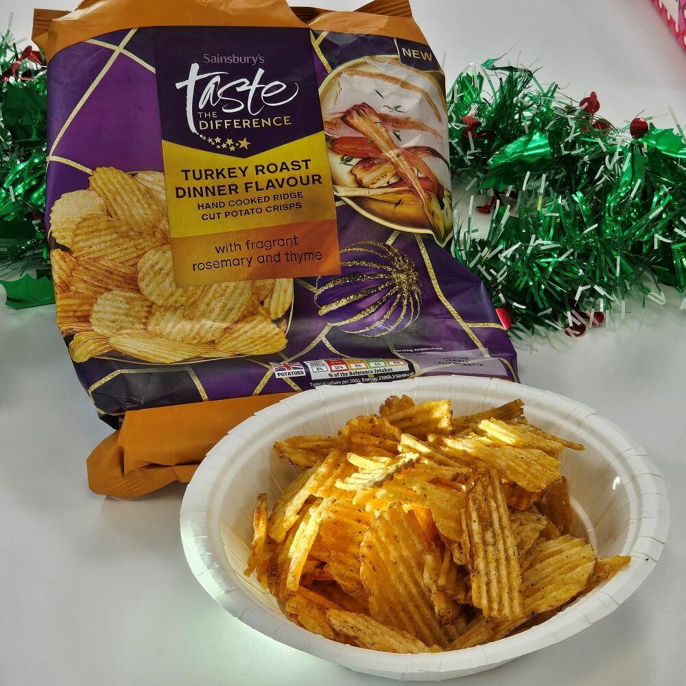 tcb sainsburys taste the difference roast turkey dinner crisps A bowl of ridged potato crisps in front of a Sainsbury's Taste the Difference Turkey Roast Dinner Flavour crisps bag, with green and red tinsel in the background.