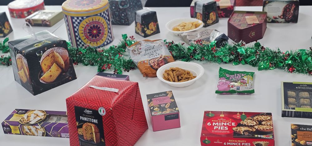 topcashback christmas snack taste test 3 A variety of packaged holiday snacks and desserts are displayed on a white table with green tinsel decorations.