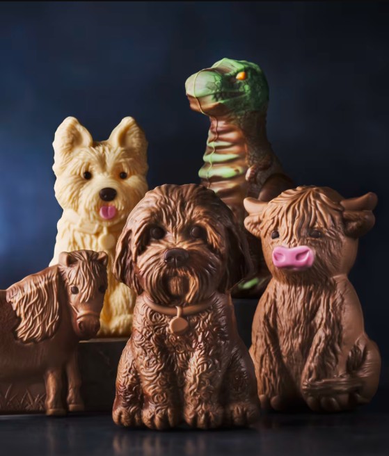 A group of chocolate figures shaped like various animals, including dogs, a cow, a horse, and a dinosaur, are arranged together against a dark background.