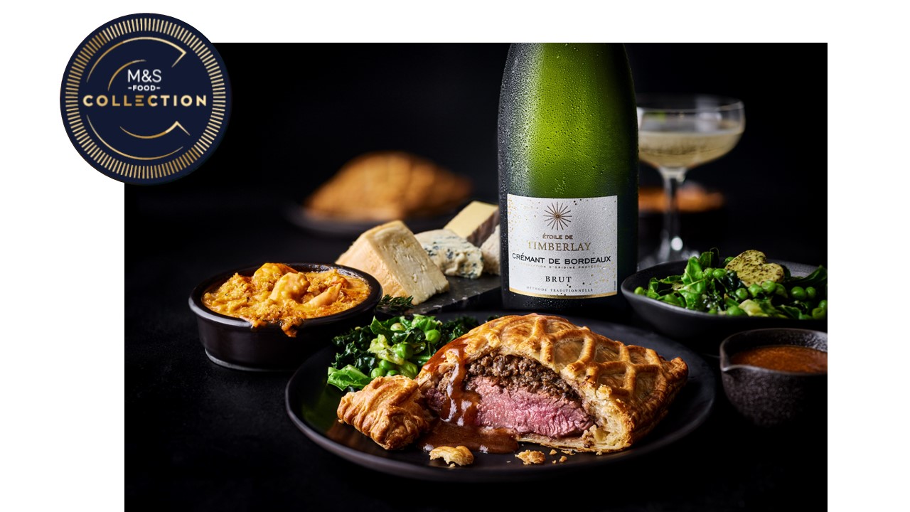 marks and spencer valentines dine in 2026 A plate with a cut beef Wellington, greens, and sauce, with cheese, a sparkling wine bottle, glass, and side dishes in the background; M&S Collection logo in the corner.