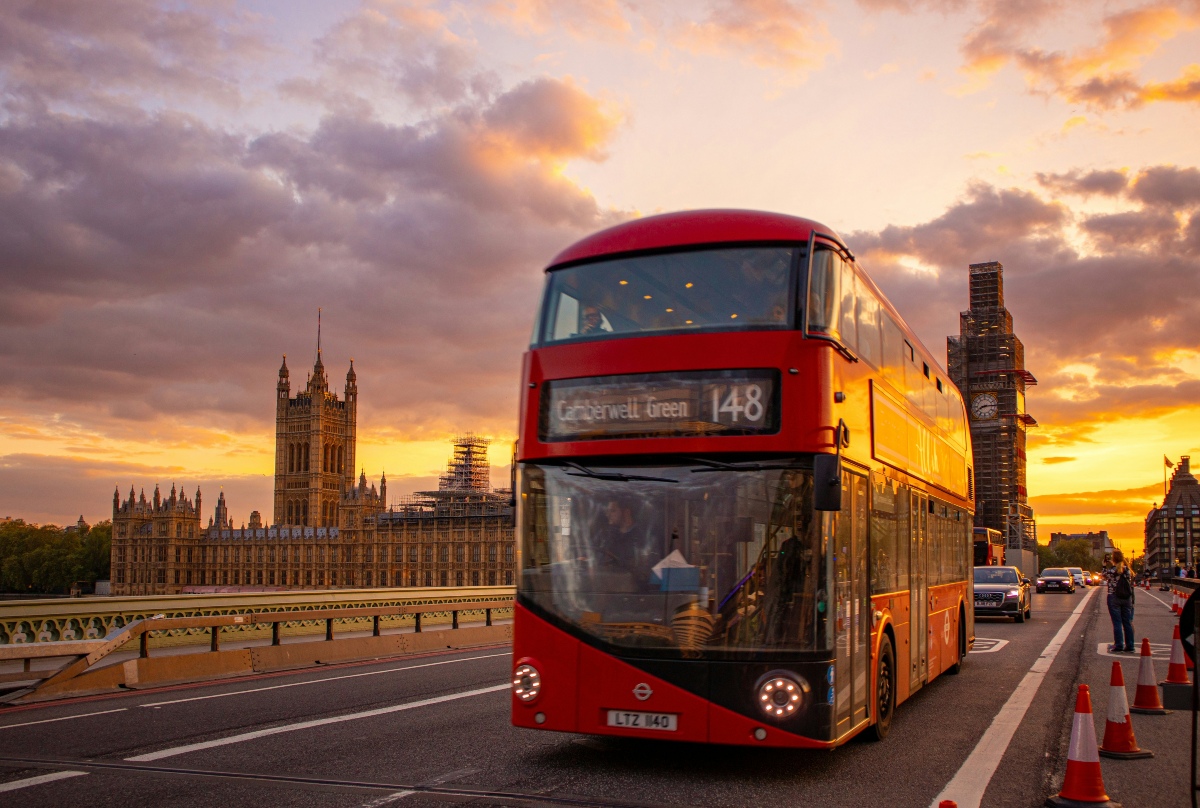 A red double-decker bus on Westminster Bridge in London at sunset, with the Houses of Parliament and Big Ben in the background.