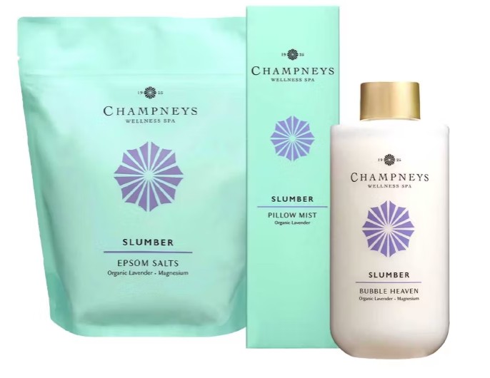 champneys bath Three Champneys Wellness Spa "Slumber" products: Epsom Salts in a pouch, Pillow Mist in a box, and Bubble Heaven in a bottle, all labeled with organic lavender and magnesium.