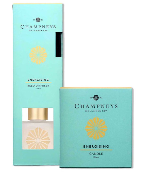 Two Champneys Wellness Spa products: an energising reed diffuser and a candle, both in aqua blue packaging with gold accents and citrus scent mentioned.